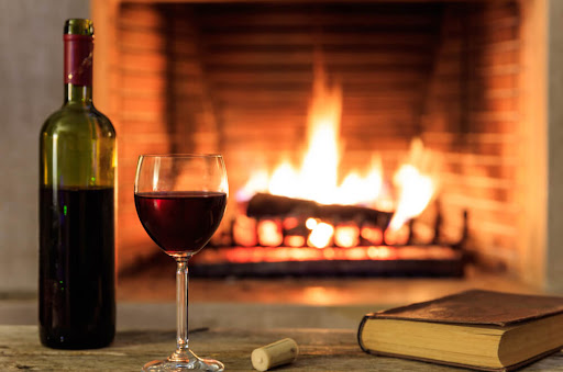 A glass of wine and a book with a cozy fireplace in the background. A romantic getaway is just one of the endless things to do in Eureka Springs for couples!

